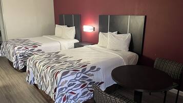 Habitación de hotel con dos camas, una mesita pequeña y una silla.