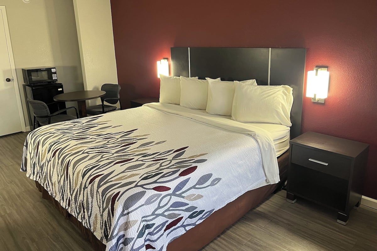 A hotel room with a bed, a desk, a chair, a microwave, and a nightstand.