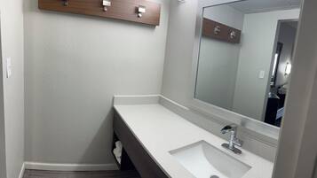 A modern bathroom with a white sink, a large mirror, and a wooden shelf above the sink.