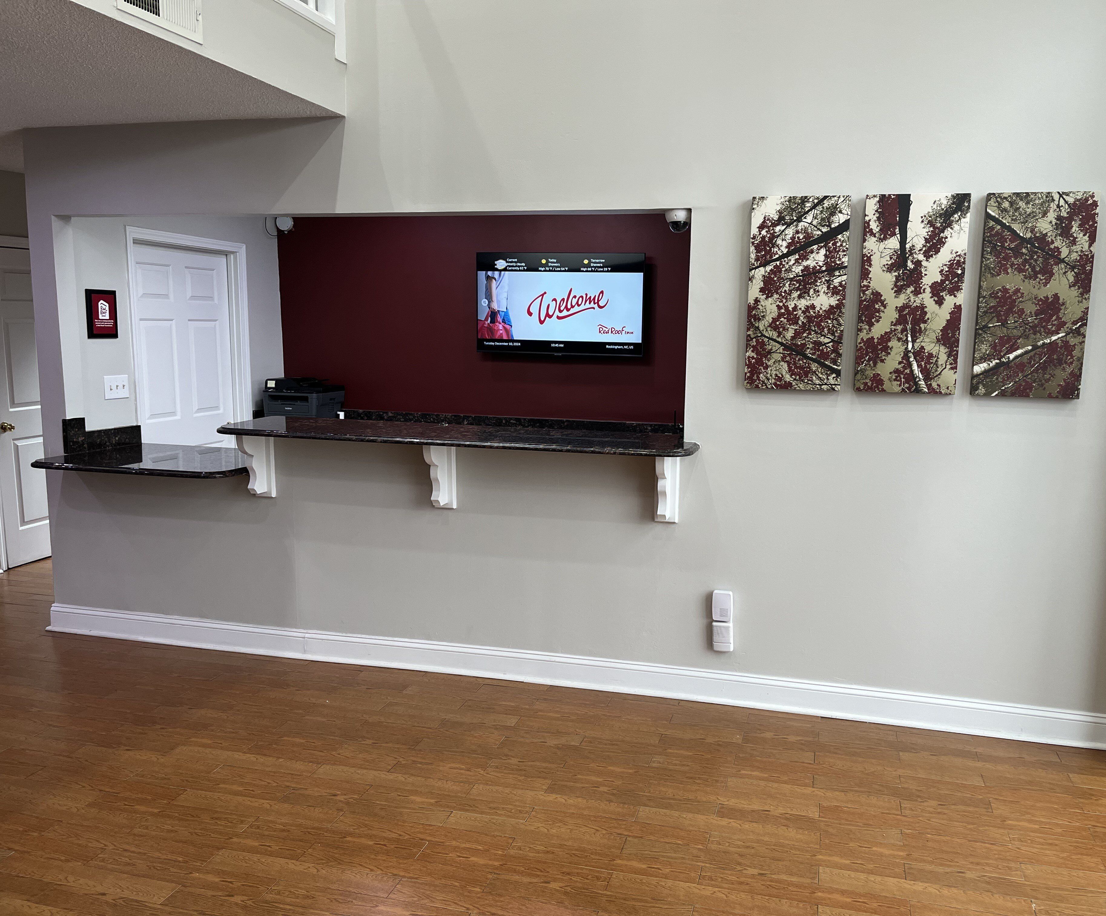 Un área de recepción con una televisión de pantalla plana, un mostrador de recepción y tres obras de arte enmarcadas en la pared.