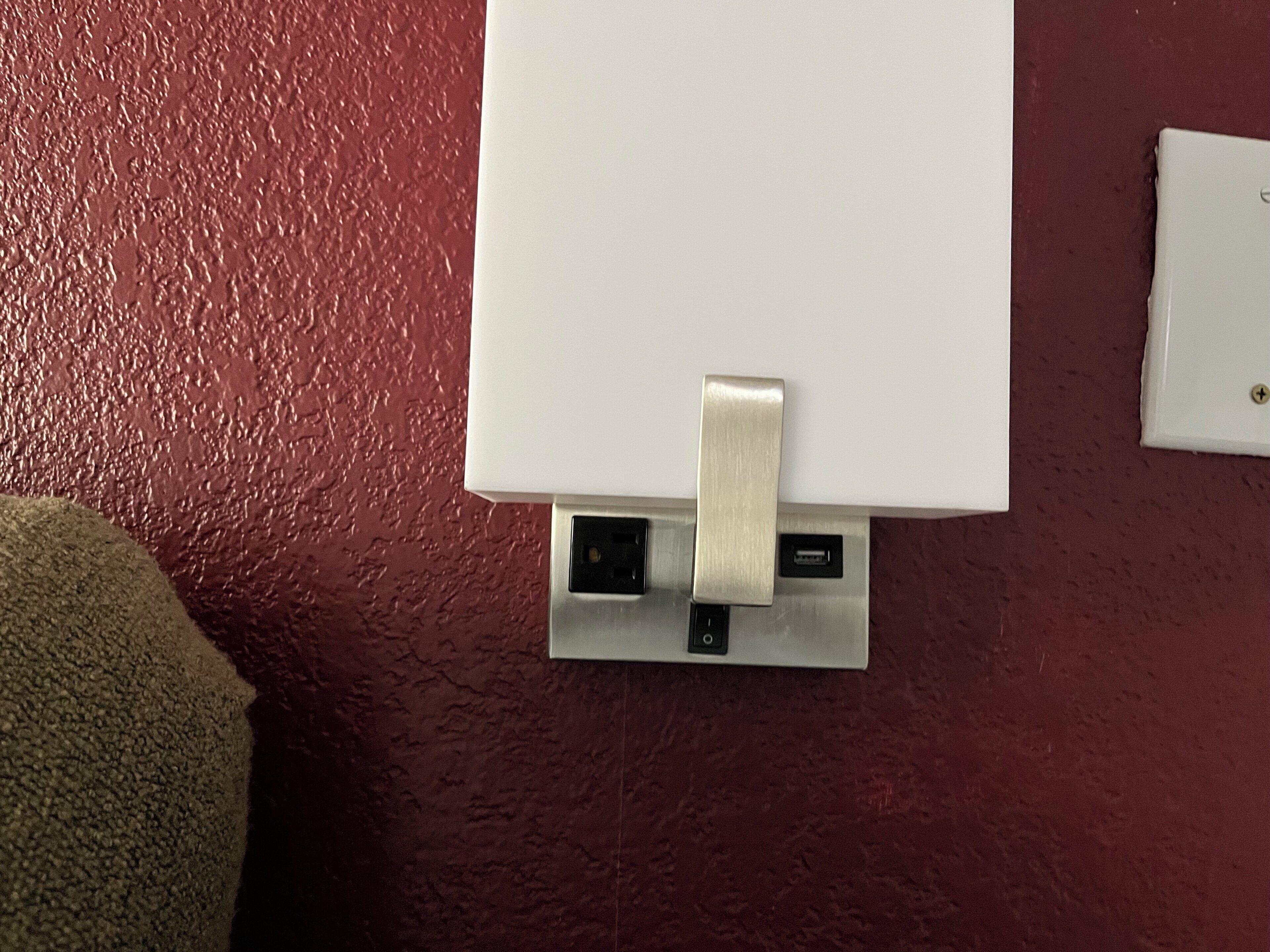 A white wall-mounted device with a USB port and a power outlet, set against a textured red wall.