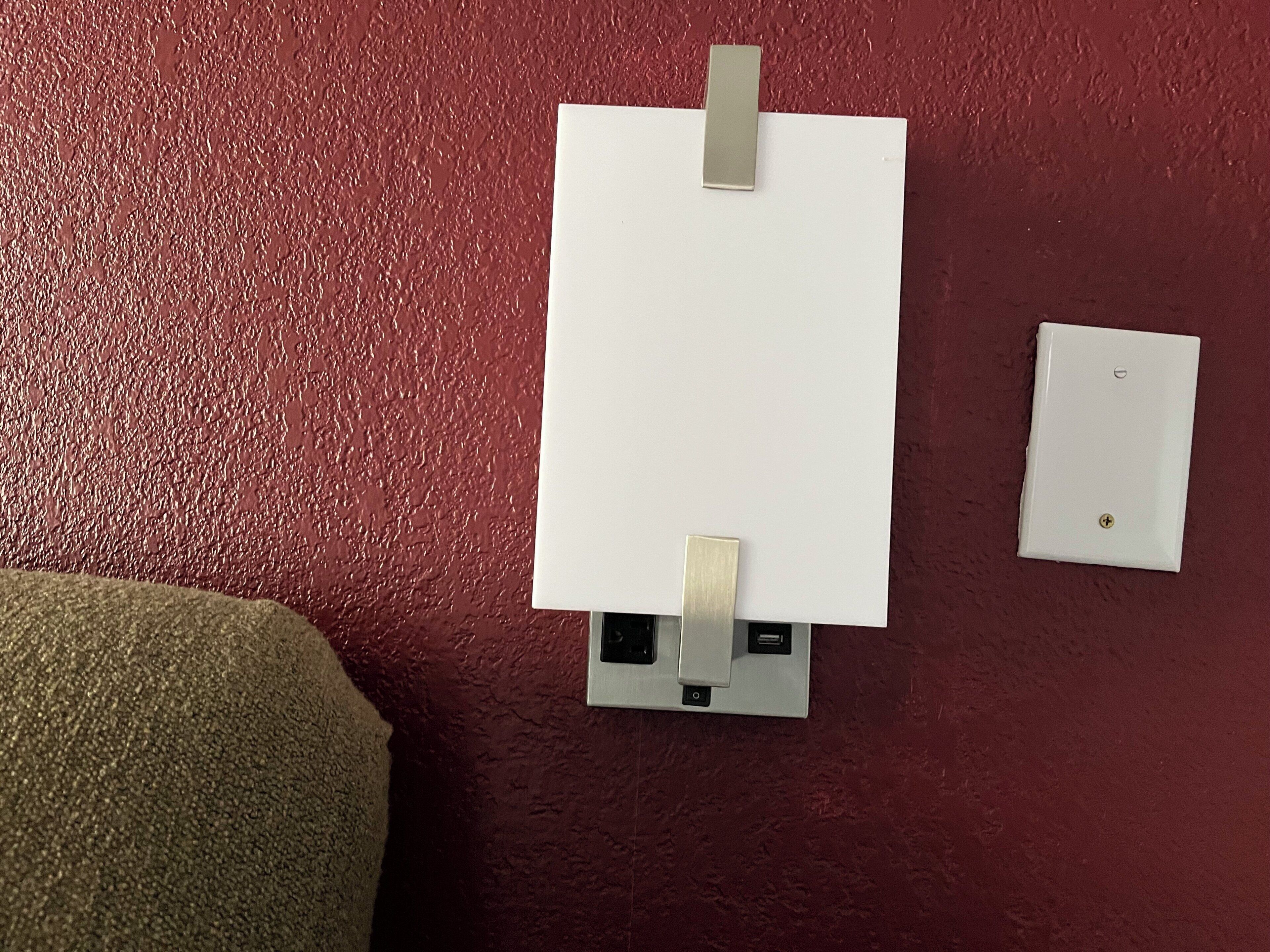 A whiteboard on a textured wall with two metal clips, a power outlet, and a light switch.