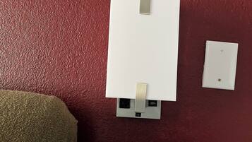 A whiteboard on a textured wall with two metal clips, a power outlet, and a light switch.