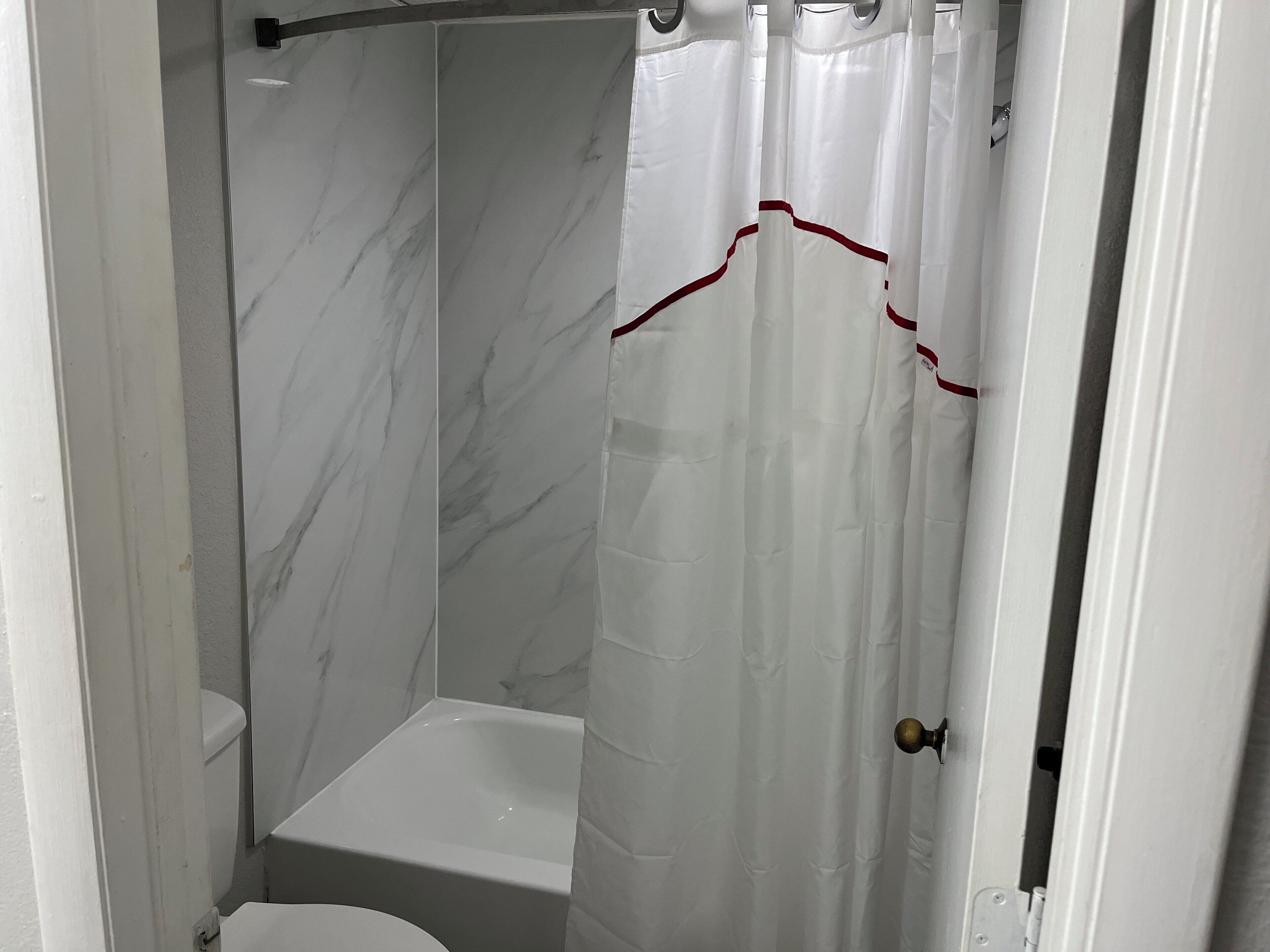 A bathroom with a white bathtub, a white toilet, and a shower curtain with a red trim.