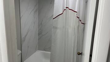 A bathroom with a white bathtub, a white toilet, and a shower curtain with a red trim.