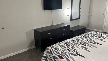 A bedroom with a bed, a dresser, a TV, and a mirror.