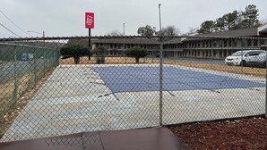 A fenced parking area with a Red Roof Inn sign, a building with a flat roof, and a white car parked nearby. - Red Roof Inn Rockingham (Rockingham)