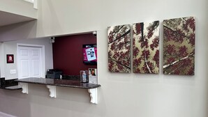 A reception area with a marble counter, a red wall, and three framed artworks depicting trees. - Red Roof Inn Rockingham (Rockingham)