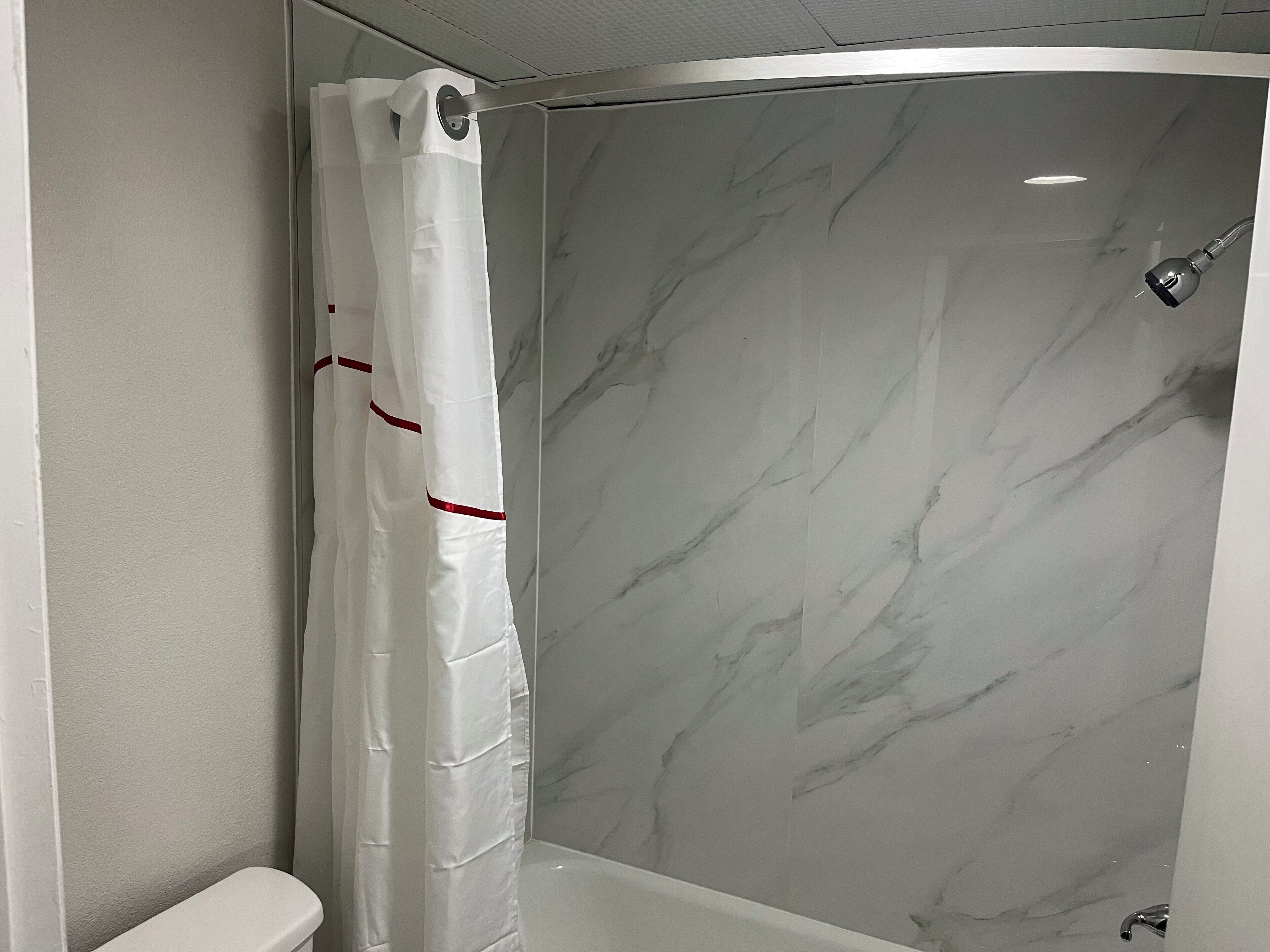 Une salle de bain avec un rideau de douche, des toilettes et des murs en marbre.