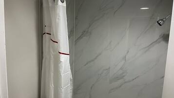 Une salle de bain avec un rideau de douche, des toilettes et des murs en marbre.