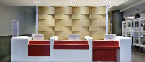 A reception area with a modern design, featuring a wooden wall panel and a counter with a red accent.