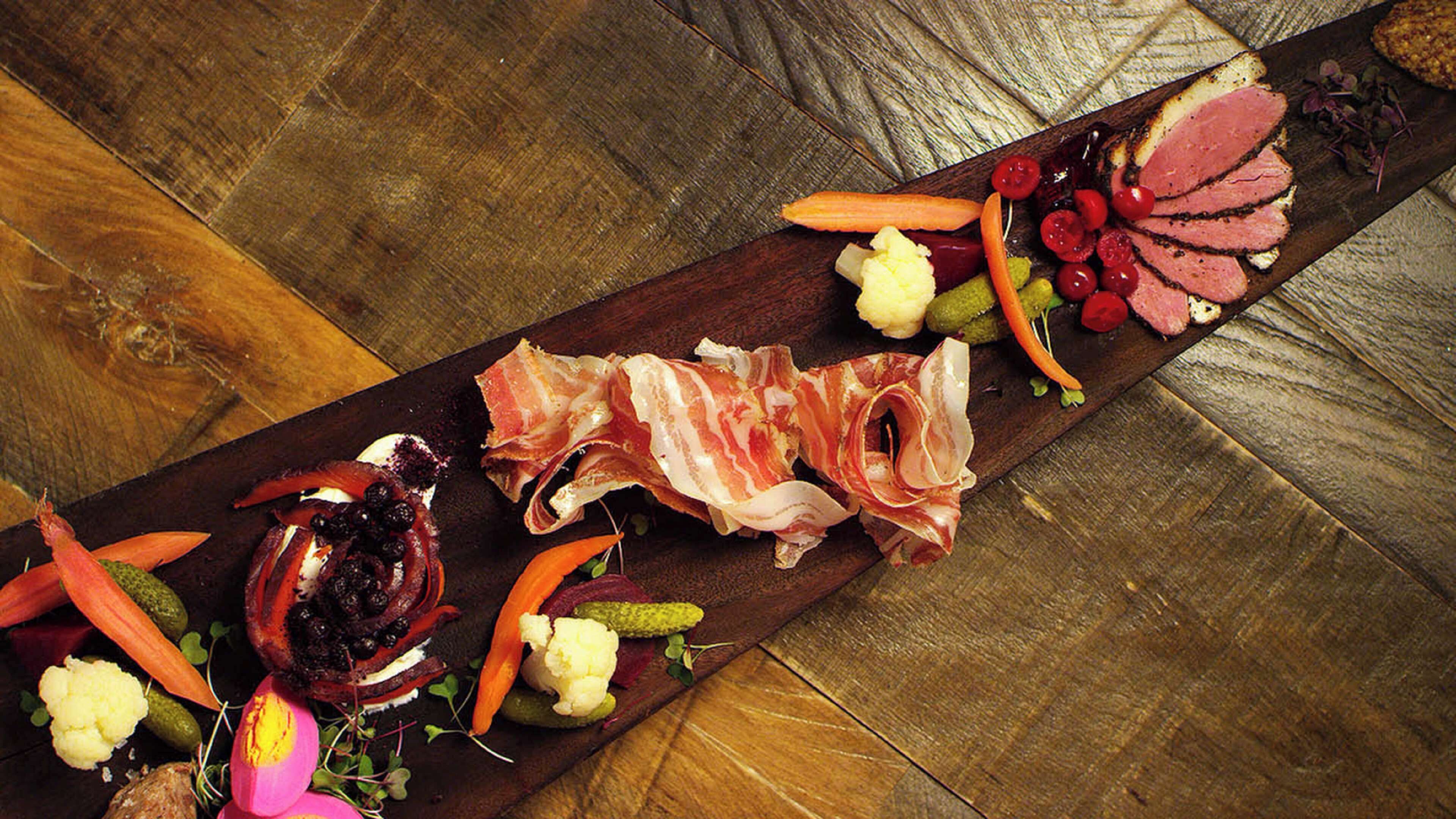 Una tabla de embutidos con diferentes carnes, quesos y verduras.