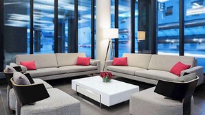 A modern lounge area with a sectional sofa, two armchairs, a coffee table, and a floor lamp. Large windows provide a view of the cityscape. - DoubleTree by Hilton Ottawa Downtown (Ottawa)