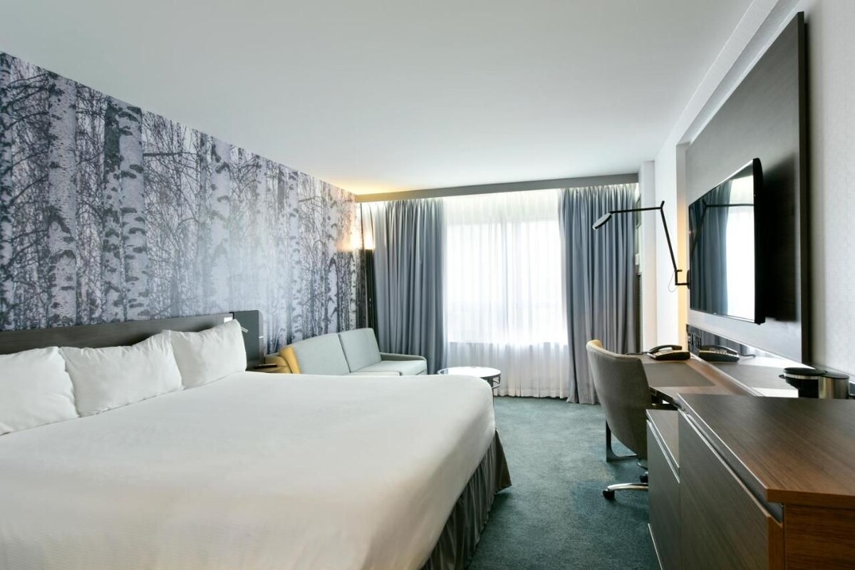 A hotel room with a large bed, a desk, a chair, a television, and a window with curtains.