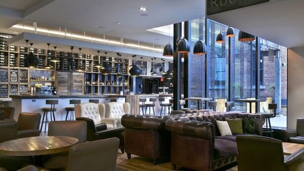 A modern bar area with leather seating, a bar counter, and a view of the city through large windows. - DoubleTree by Hilton Ottawa Downtown (Ottawa)