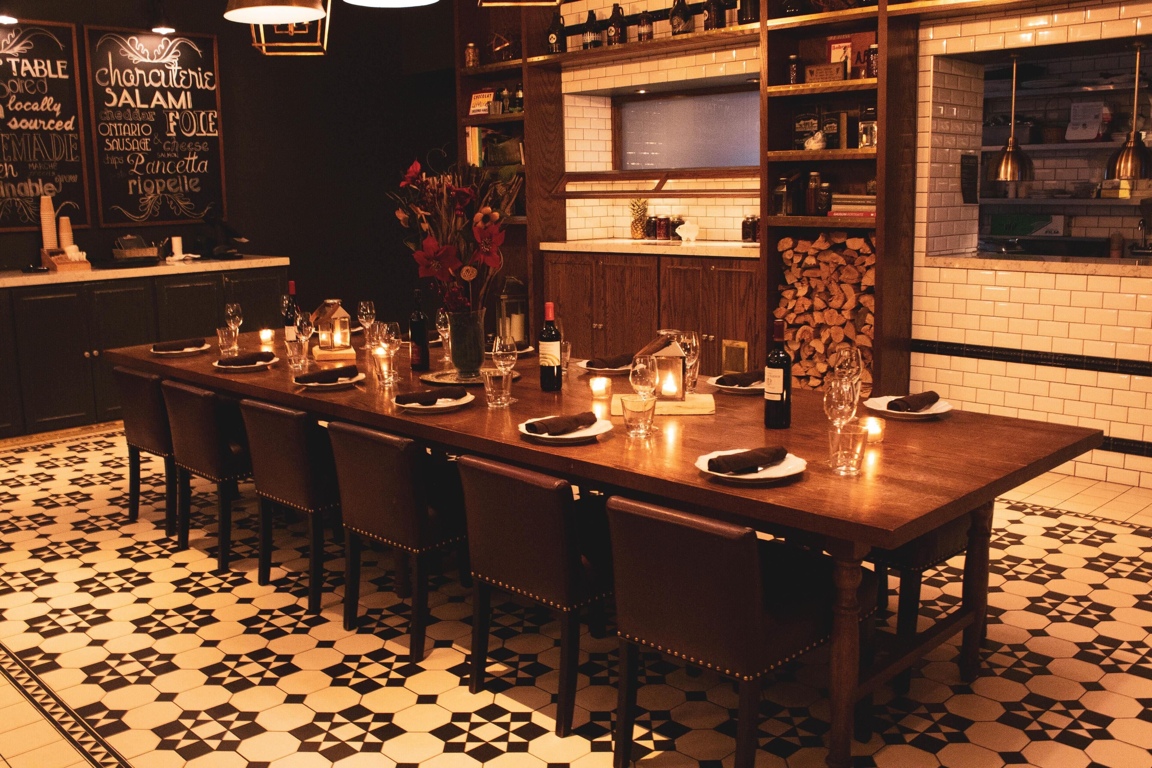 Un comedor con una mesa de madera larga dispuesta para seis personas, rodeada de sillas. El piso tiene un patrón de baldosas geométricas en blanco y negro.