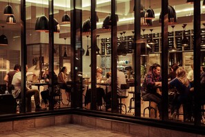 An indoor dining area with multiple tables and chairs, large windows, and hanging pendant lights. - DoubleTree by Hilton Ottawa Downtown (Ottawa)