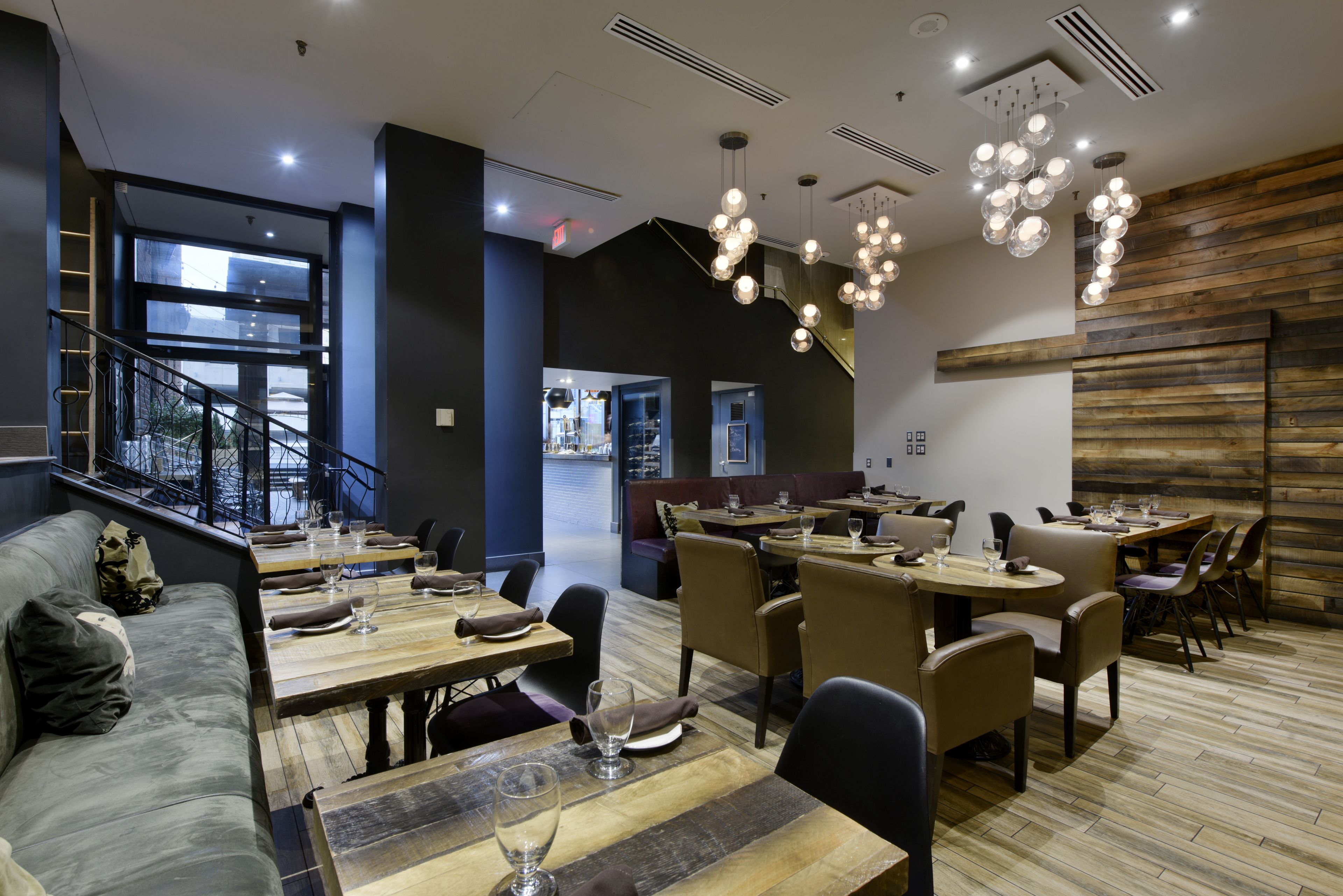 Un restaurante moderno con mesas y sillas de madera, una escalera y vistas a la ciudad.