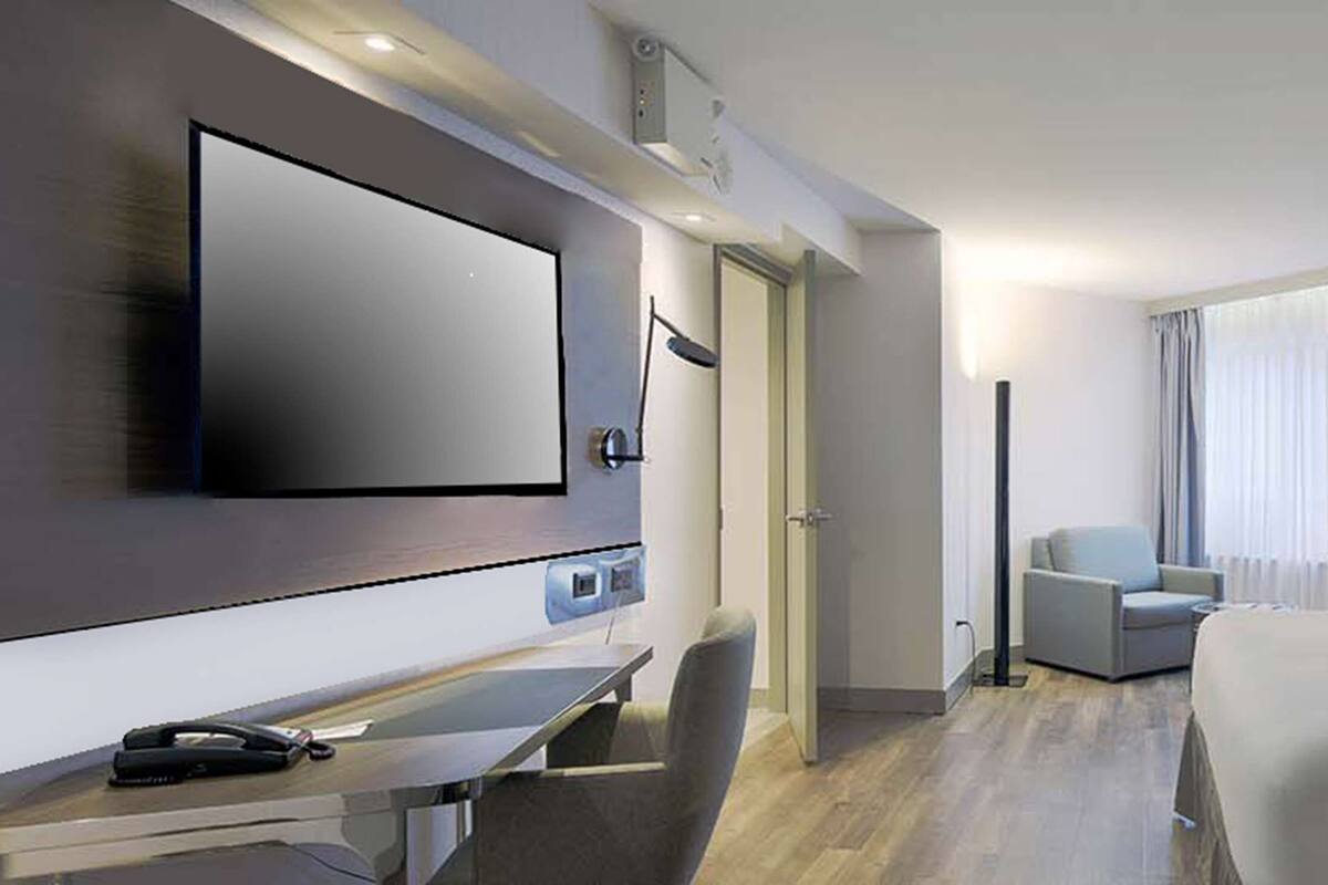 Una habitación de hotel moderna con una cama grande, un televisor de pantalla plana montado en la pared, un escritorio con un teléfono y una silla.