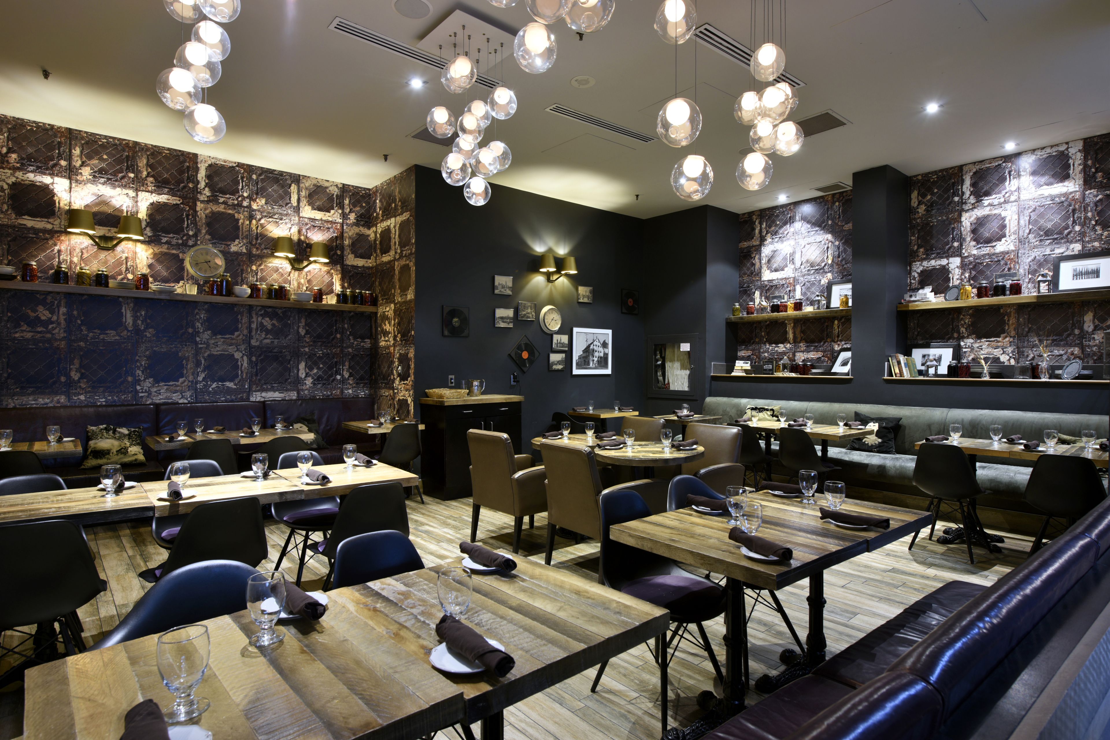Um restaurante com mesas e cadeiras de madeira, um espaço de bar e uma parede com quadros e um relógio.