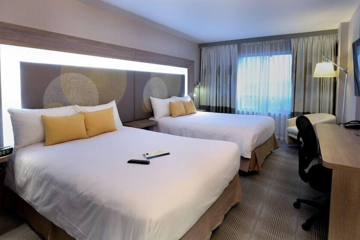 Una habitación de hotel con dos camas, un escritorio, una silla, un televisor y un ventanal con cortinas.