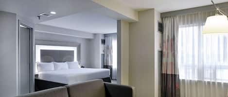 A hotel room with a bed, a sofa, a desk, and a window with curtains.