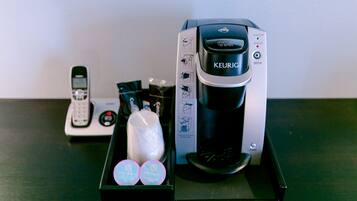 Eine Kaffeemaschine von Keurig mit Auffangtablett, einer Fernbedienung und zwei Kapseln für Keurig auf einem Tisch.