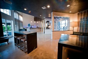 A modern hotel lobby with a reception desk, seating area, and a staircase leading to upper floors. - Hotel Current (Long Beach)