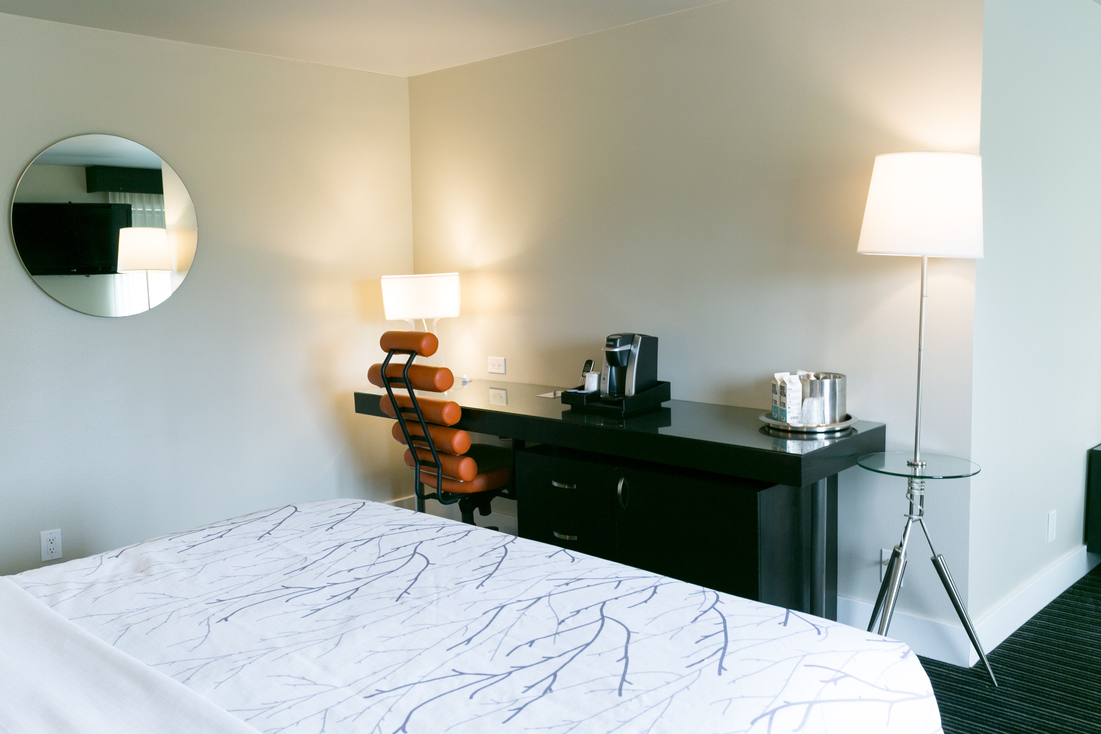 Et hotelværelse med en seng, et skrivebord med lampe, en stol og et spejl.