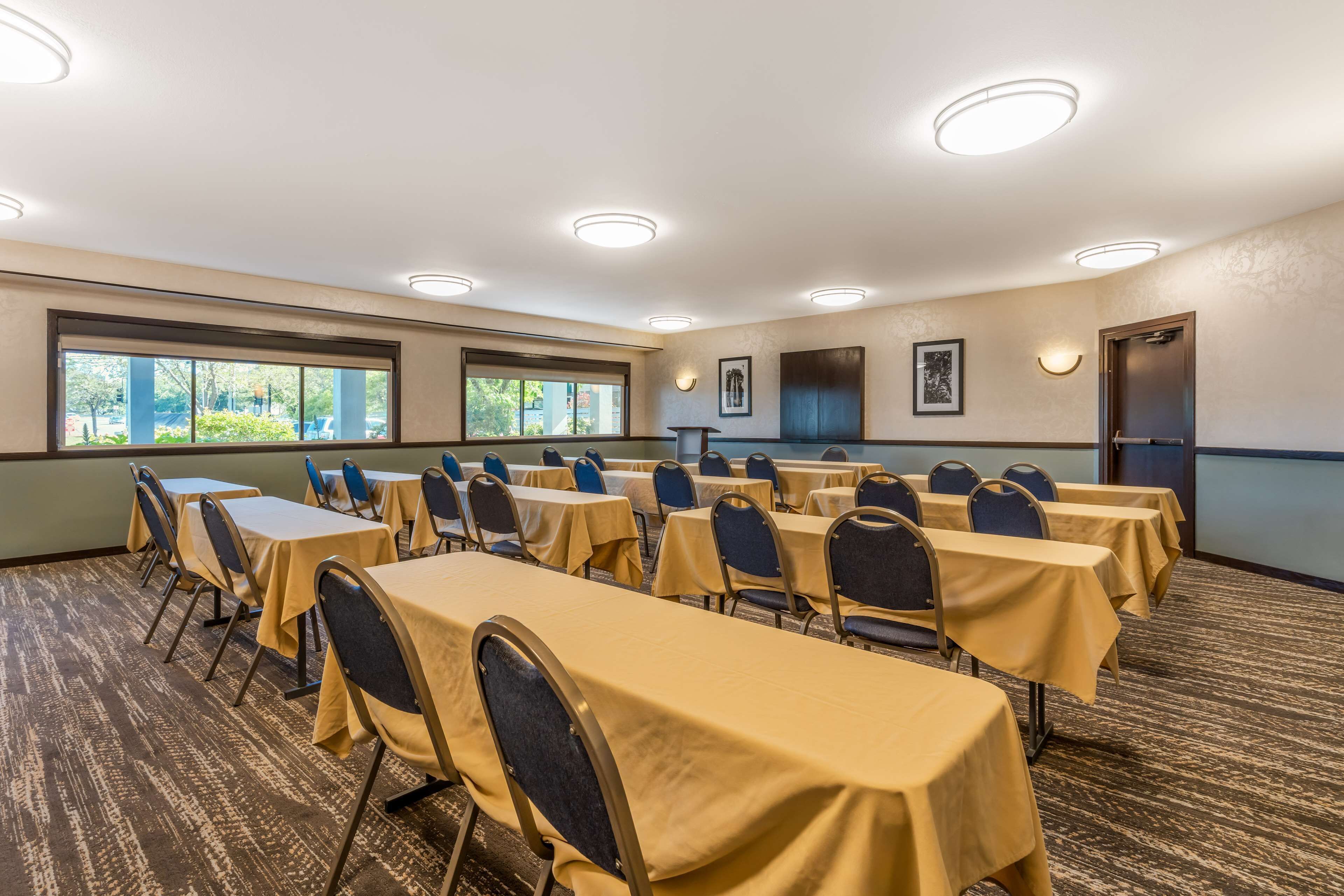 Un salón de conferencias con varias mesas y sillas, ventanas amplias e iluminación en el techo.