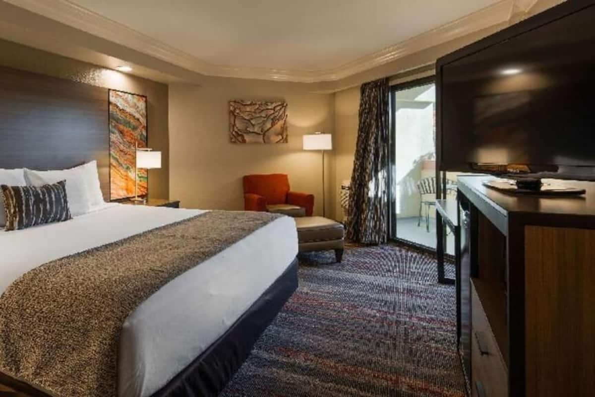 A hotel room with a large bed, a desk with a flat-screen TV, a chair, and a window with curtains.