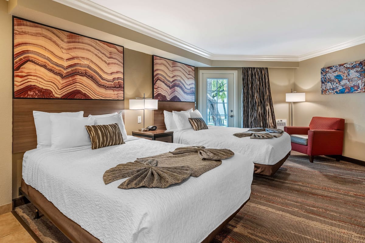 A hotel room with two beds, a red armchair, and artwork on the walls.