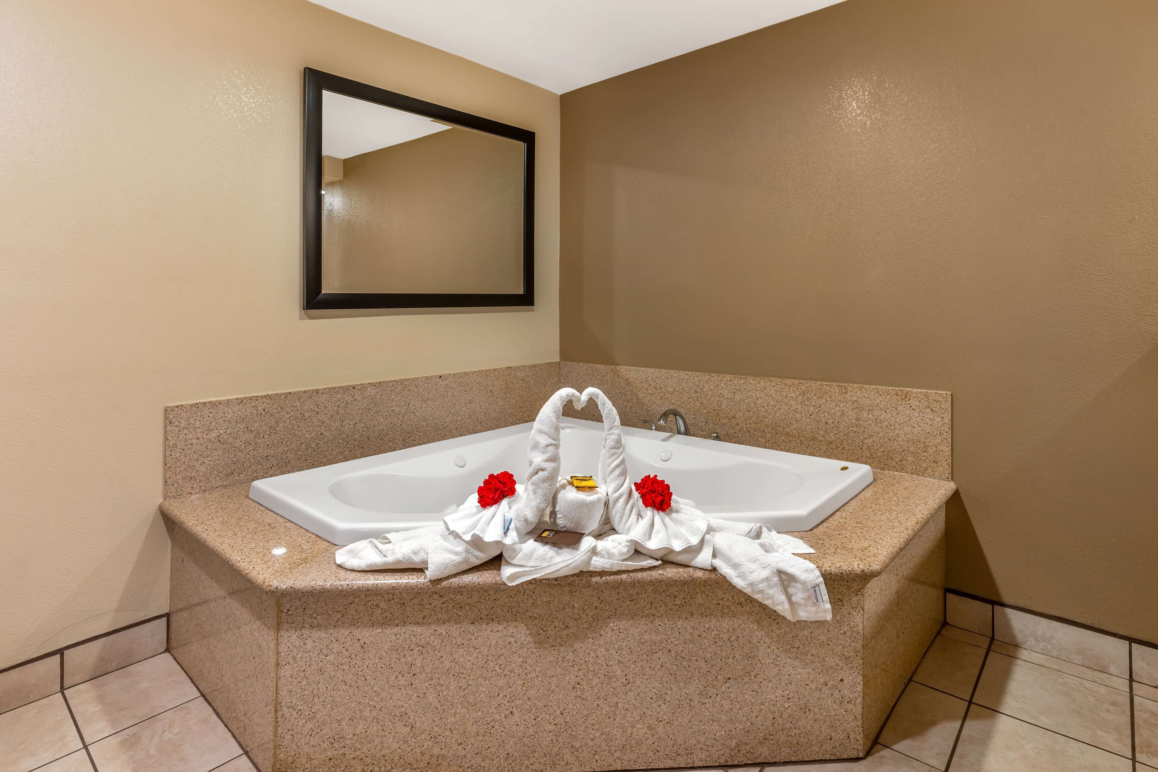 A bathroom with a large bathtub, a mirror, and towels with red flowers on the side.