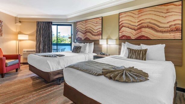 A hotel room with two beds, a red armchair, a large window with a view, and abstract wall art. - Best Western Plus Wine Country Inn & Suites (Santa Rosa)