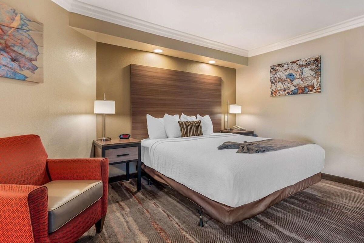 Ein Hotelzimmer mit einem großen Bett, einem roten Sessel, zwei Nachttischen mit Lampen und Bildern an den Wänden.