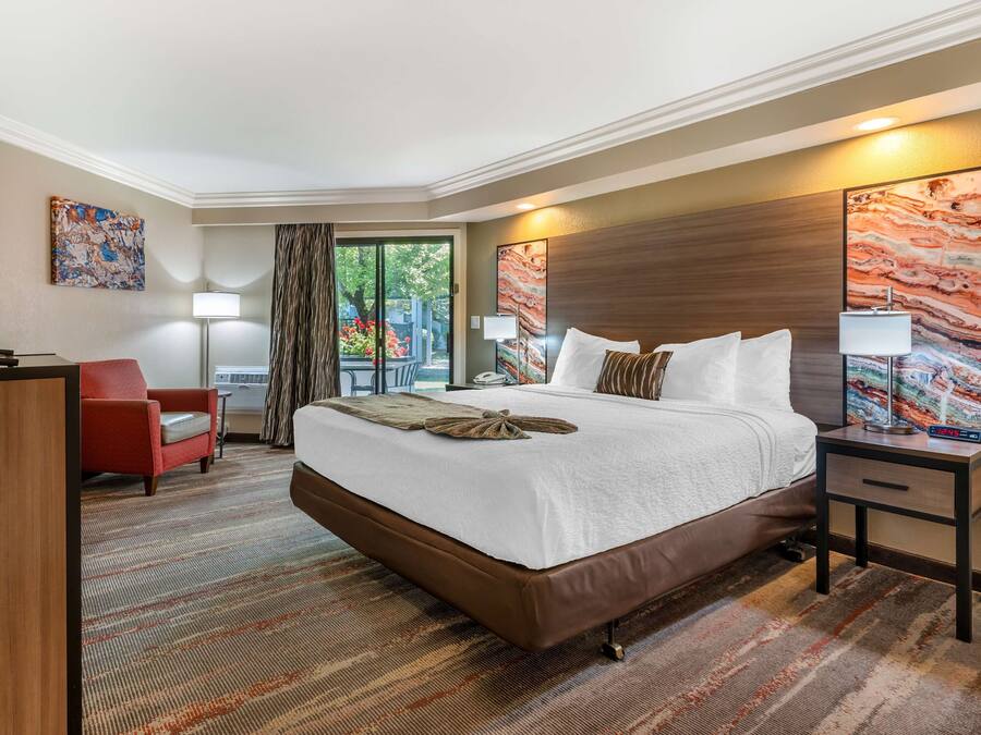 A hotel room with a large bed, a desk, a chair, and artwork on the walls.