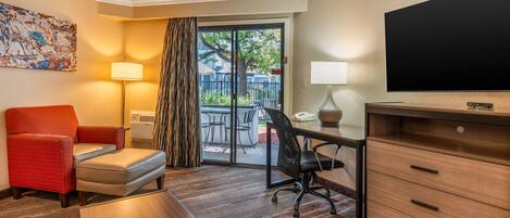 A hotel room with a red armchair, a desk with a lamp, a television, and a view of the outdoors through a sliding glass door.
