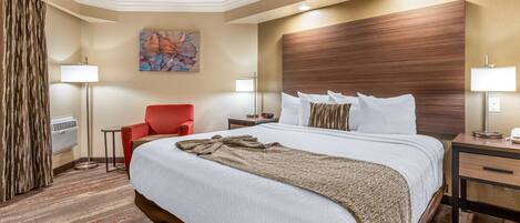 A hotel room with a large bed, a red armchair, a small table, and a painting on the wall.
