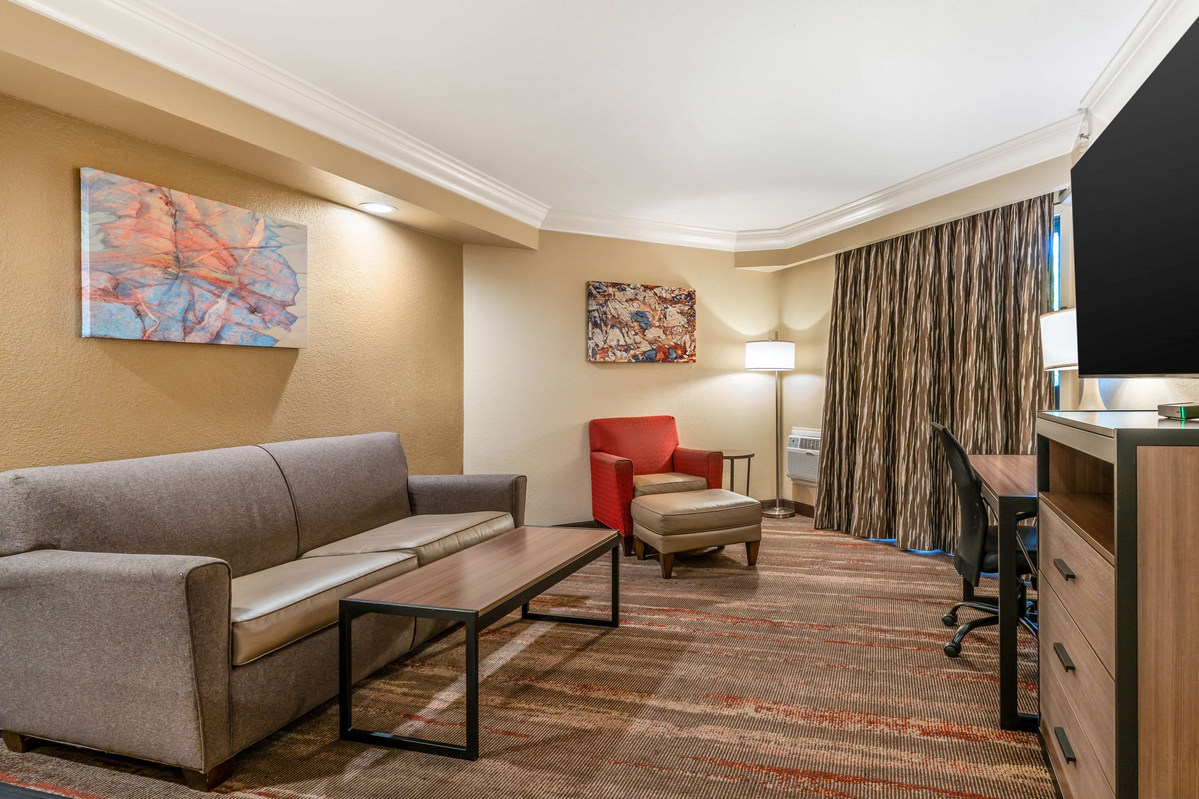 Une chambre d’hôtel équipée d’un canapé, d’un fauteuil, d’un bureau, d’une lampe et d’œuvres d’art accrochées aux murs.