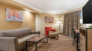 A hotel room with a sofa, armchair, desk, lamp, and artwork on the walls.
