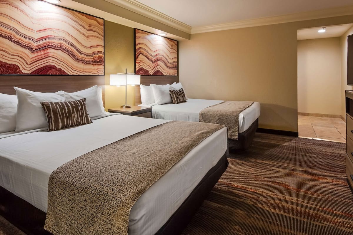 A hotel room with two beds, a TV, a dresser, and artwork on the walls.