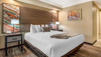 Quarto de hotel com uma cama grande, duas mesas de cabeceira, um criado-mudo e uma luminária na parede.