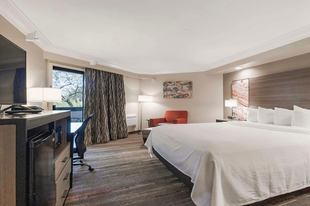 Ein Hotelzimmer mit einem großen Bett, einem Schreibtisch mit Telefon, einem Sessel und einem Fernseher.