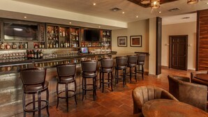 A bar area with a long counter, multiple stools, and a television screen. - Rancho Viejo Resort and Country Club (Olmito)