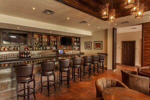 A bar area with a long counter, multiple stools, and a television screen. - Rancho Viejo Resort and Country Club (Olmito)