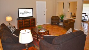 A living room with a television displaying 'Rancho Viejo Resort & Country Club', a sofa, a coffee table, and a lamp. - Rancho Viejo Resort and Country Club (Olmito)