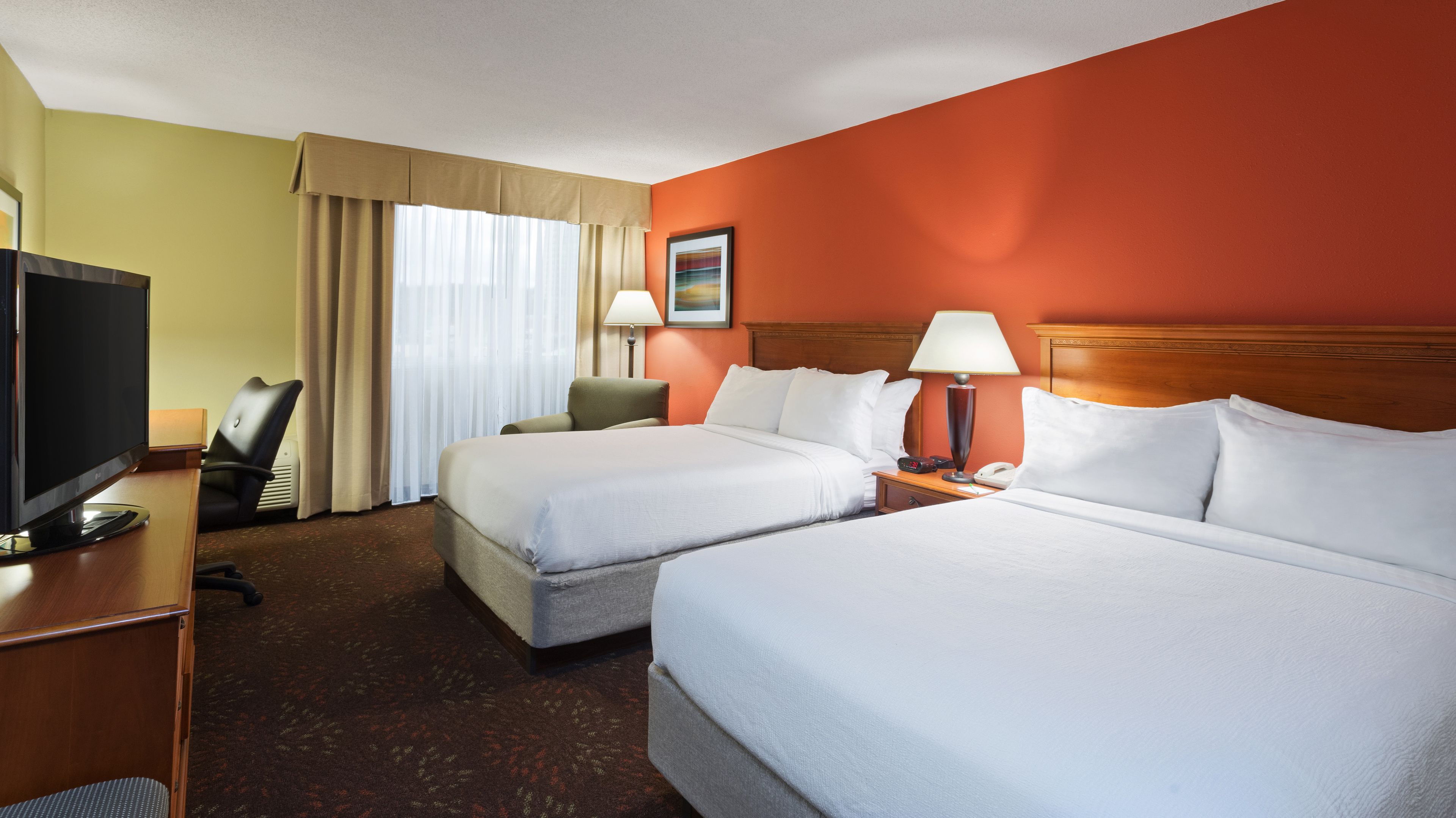 A hotel room with two beds, a desk with a TV, a chair, a lamp, and a painting on the wall.