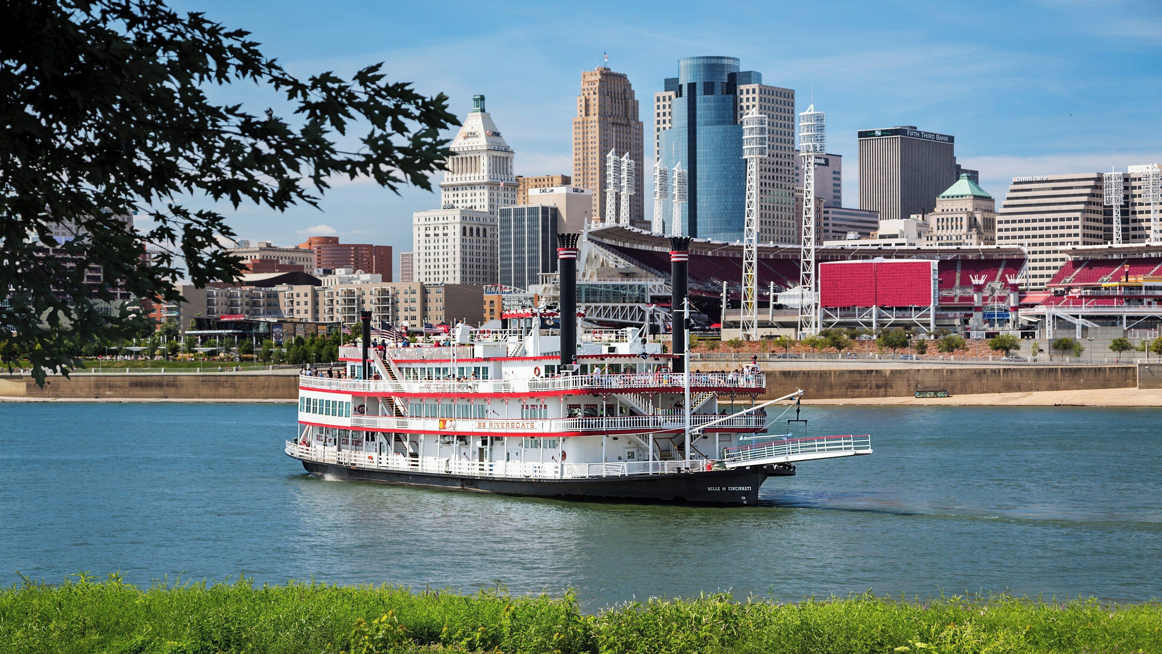 Un bateau fluvial à plusieurs ponts, arborant une livrée blanche et rouge, était amarré près de la silhouette d’une ville, avec ses différents bâtiments et son stade.