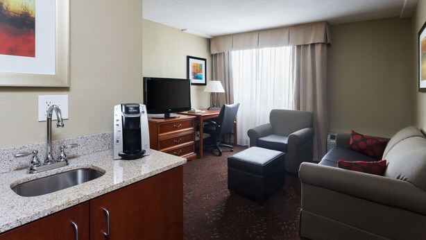 A hotel room with a kitchenette, a flat-screen TV, a desk, a chair, a sofa, and a window with curtains. - Holiday Inn Cincinnati-Riverfront by IHG (Covington)
