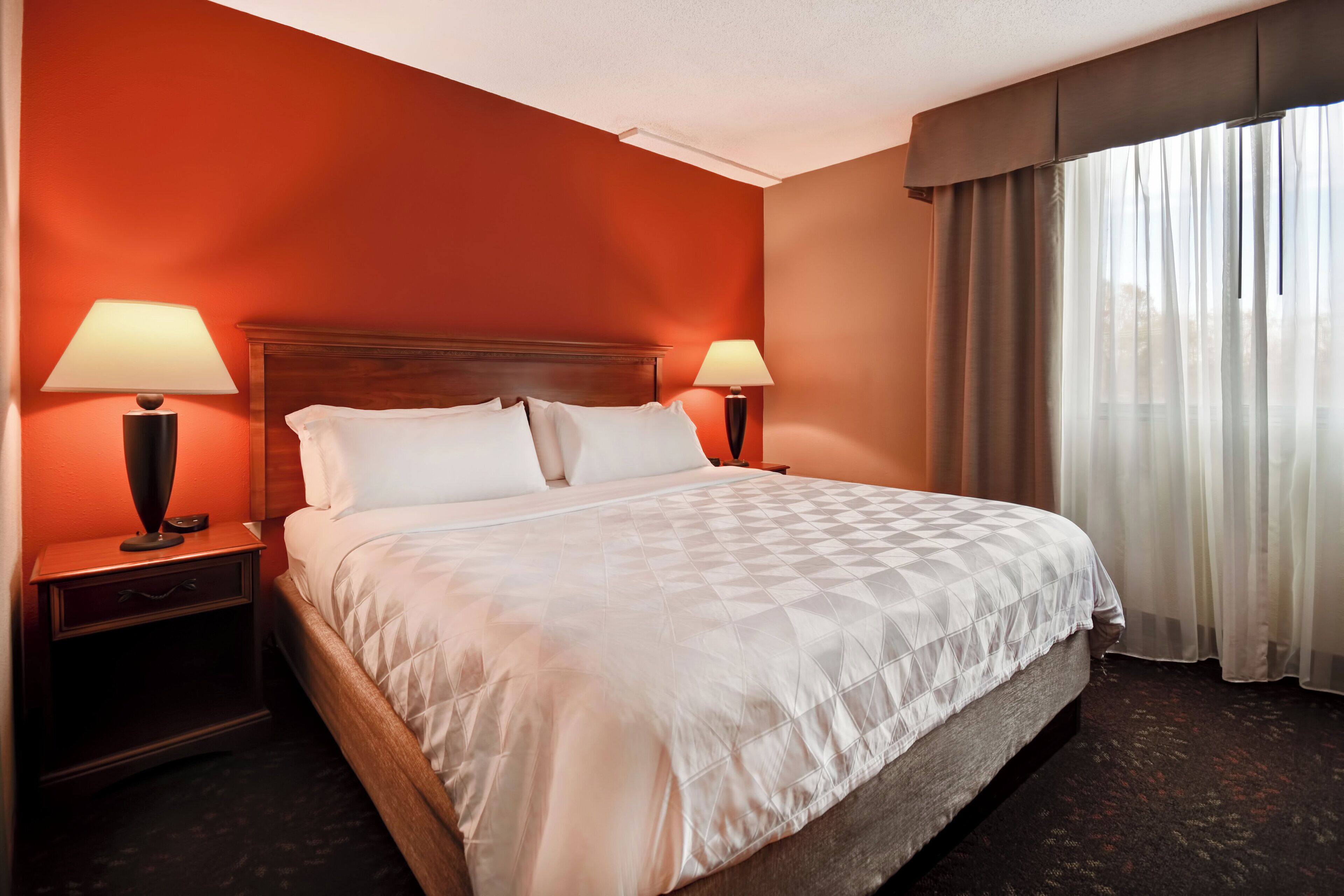 Een hotelkamer met een groot bed, twee nachtkastjes met lampen en een raam met gordijnen.